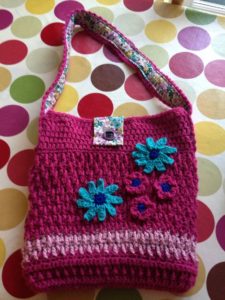 A pink crocheted shopping bag fabric lined and decorated with crochet flowers.