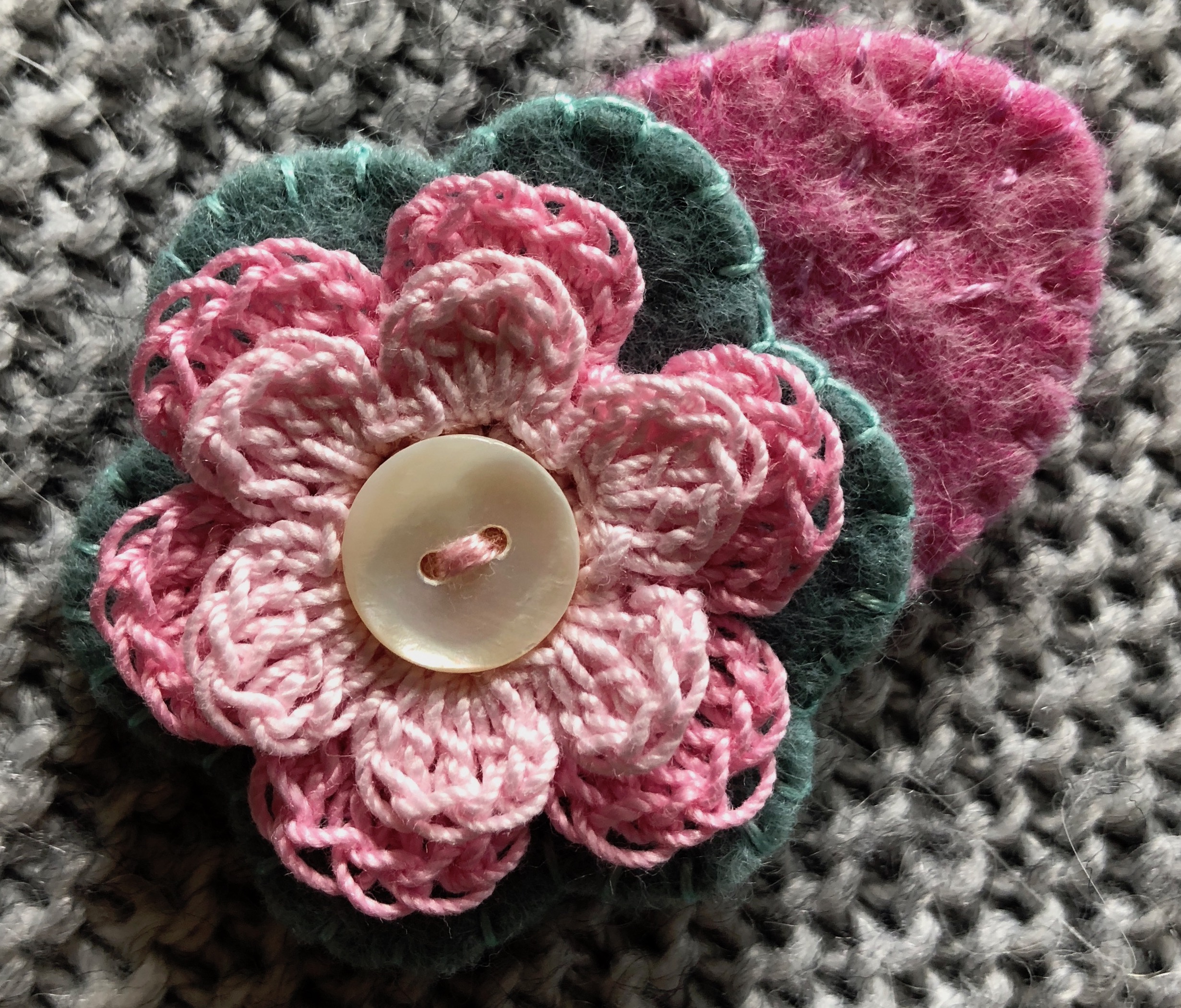 Small hand stitched felt and crocheted flower brooch in pink sand pale grey with mother of pearl button centre.