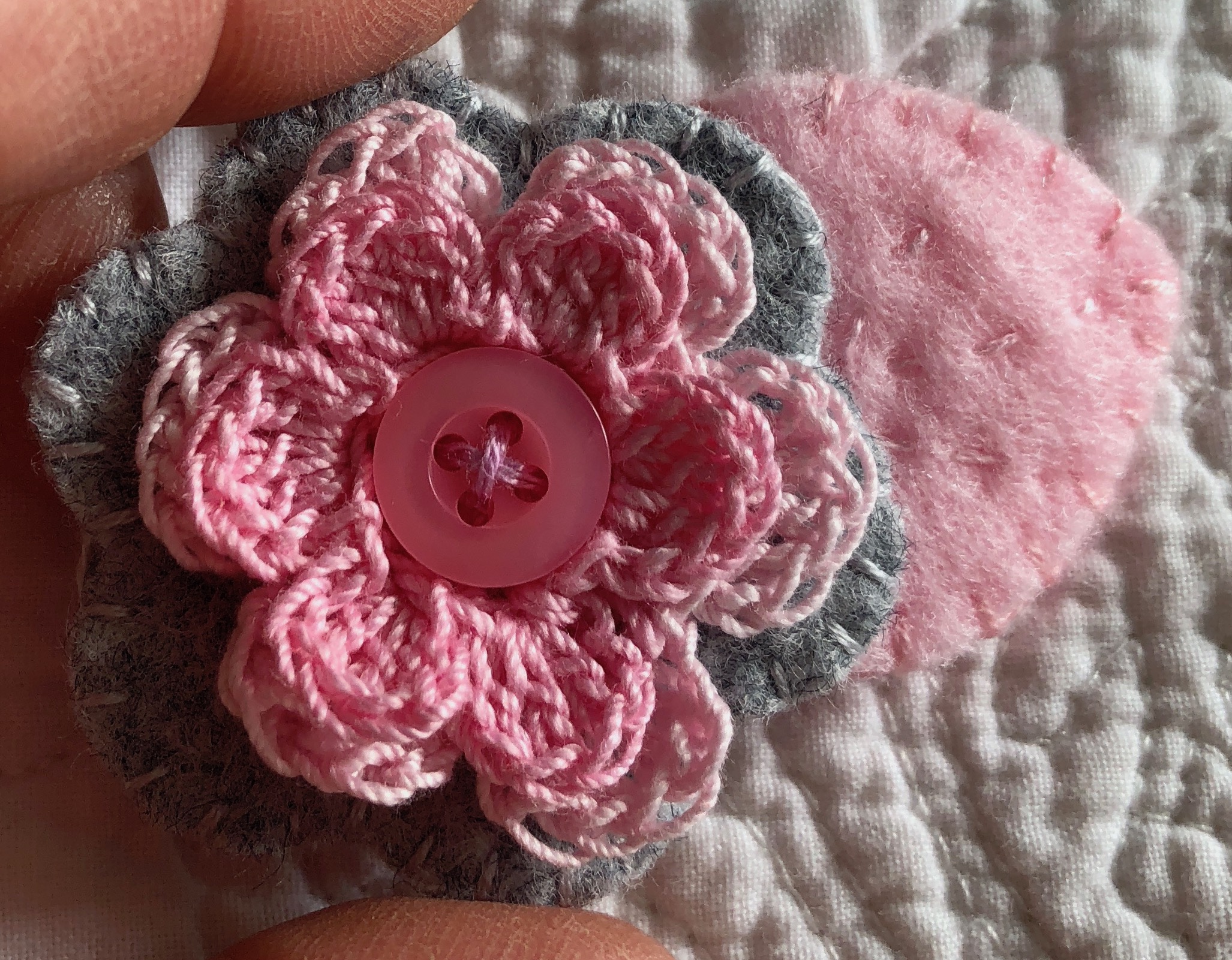 Small hand stitched felt and crocheted flower brooch in pinks and pale grey with a pink button centre.
