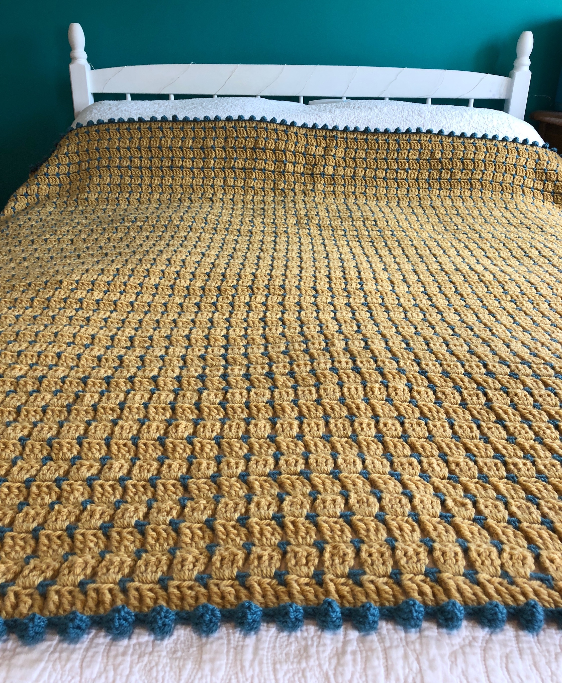 Block stitch blanket in mustard yellow and teal, with pom-pom edging.