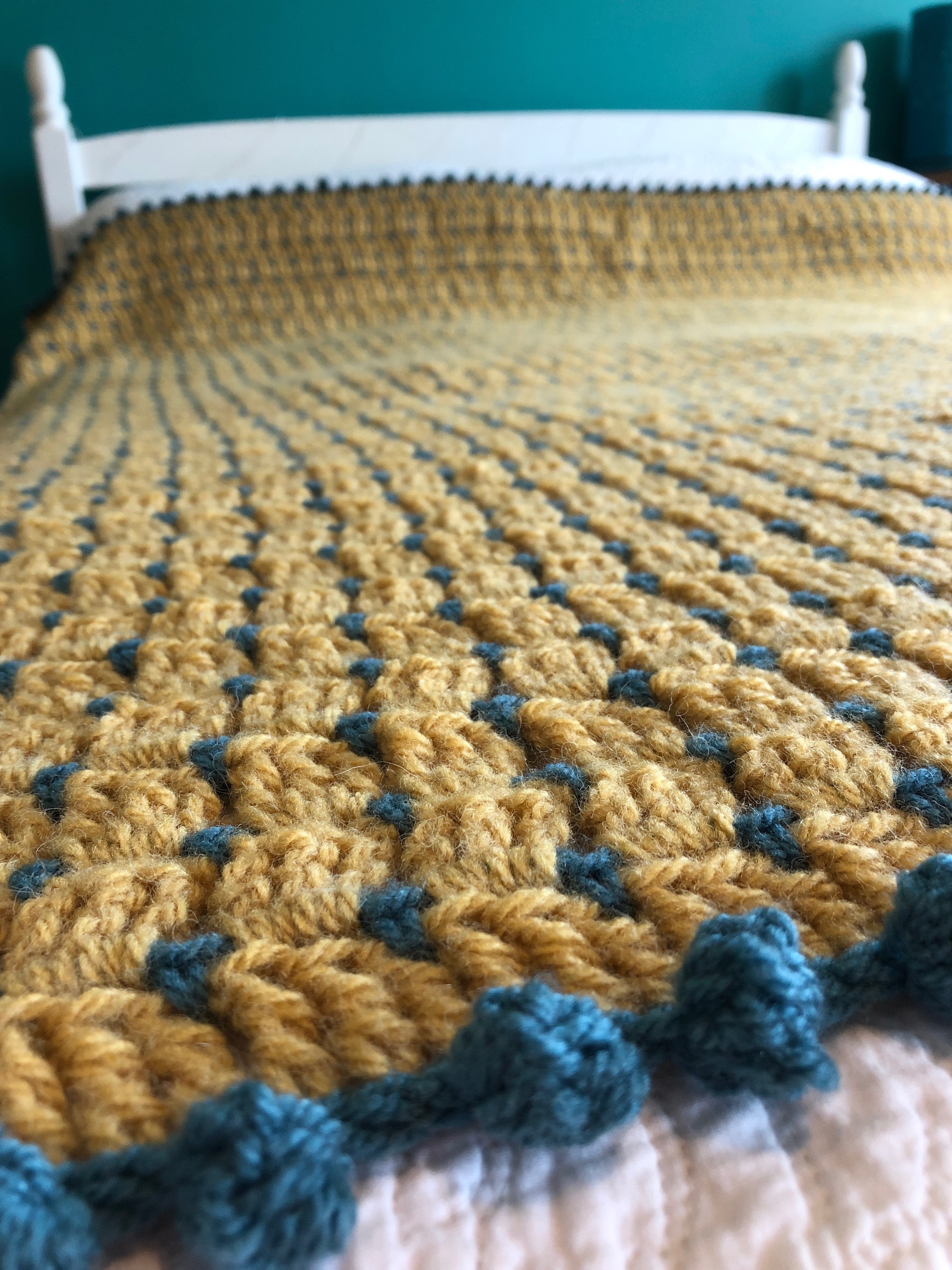 Block stitch blanket in mustard yellow and teal, with pom-pom edging.