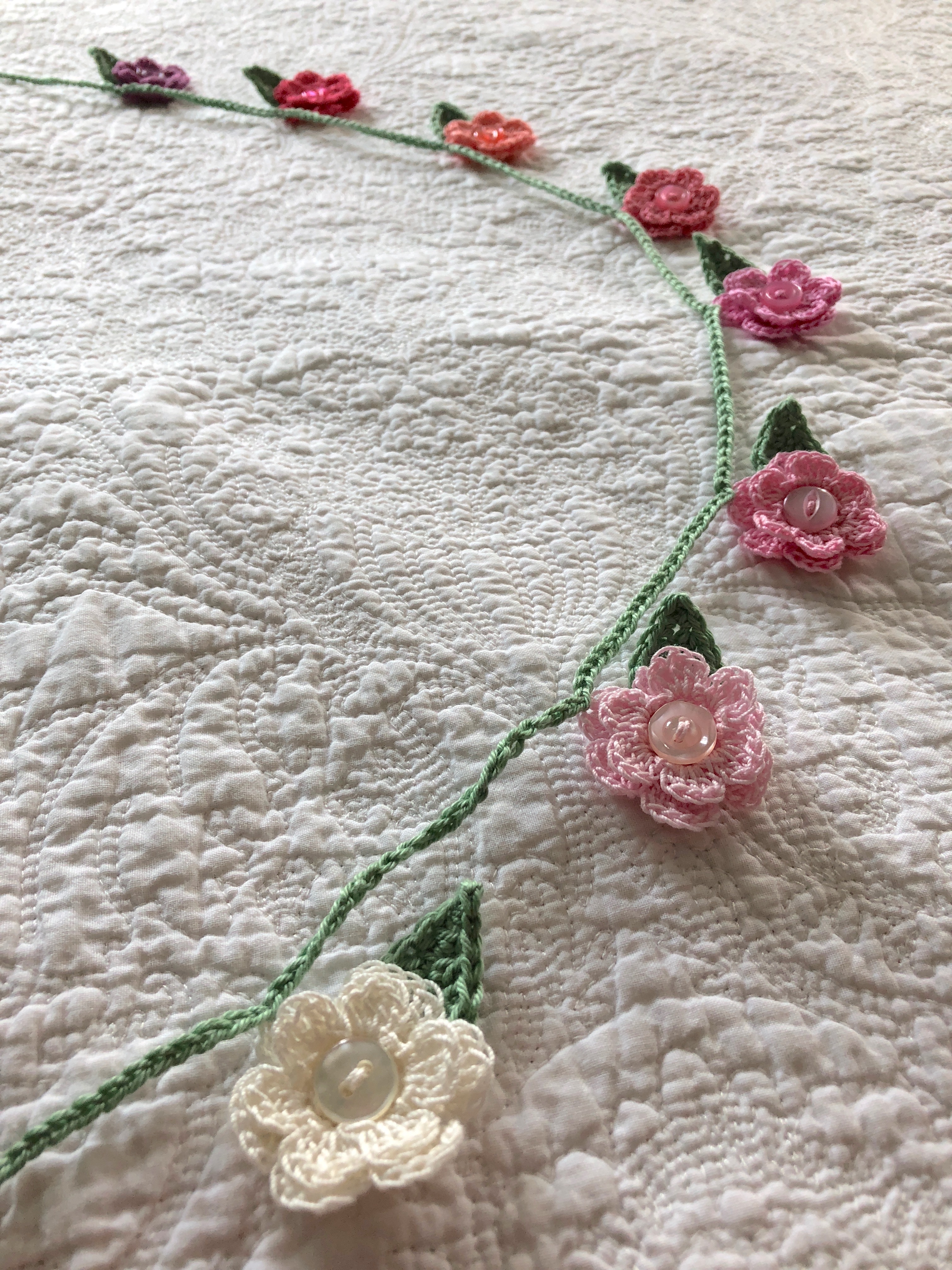 A hand crocheted small flower and leaf garland in graduated colour way from white through pinks to purple.