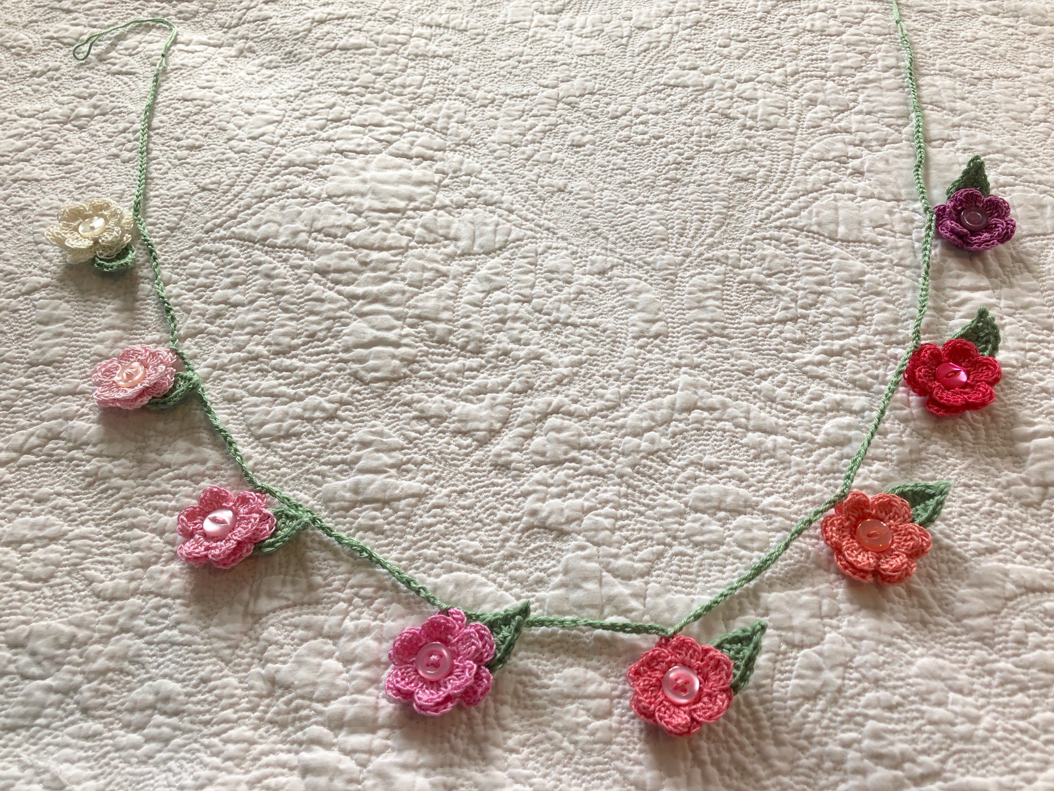 A hand crocheted small flower and leaf garland in graduated colour way from white through pinks to purple.