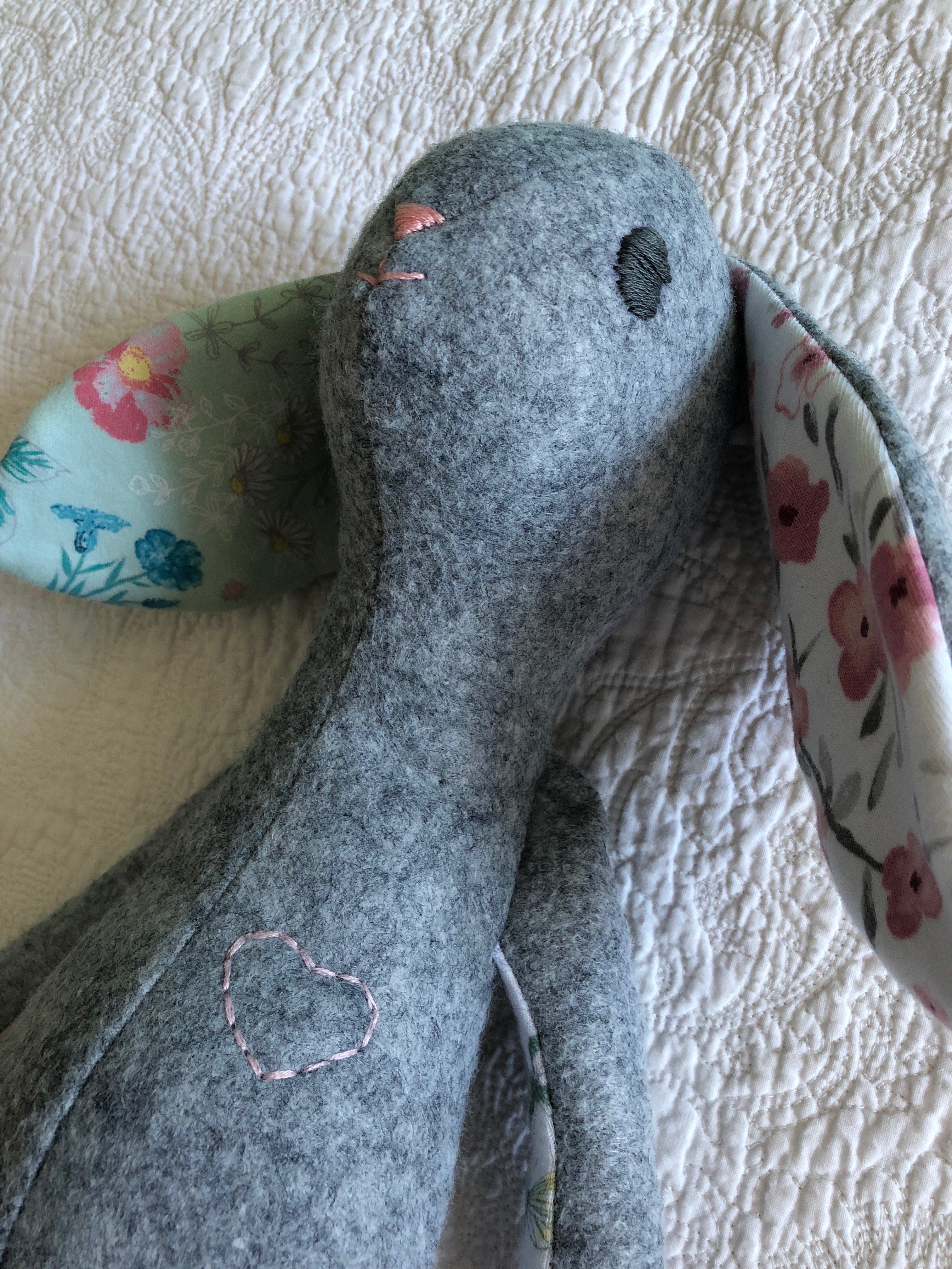 A grey felt and multi fabric keepsake bunny with hand embroidered details.