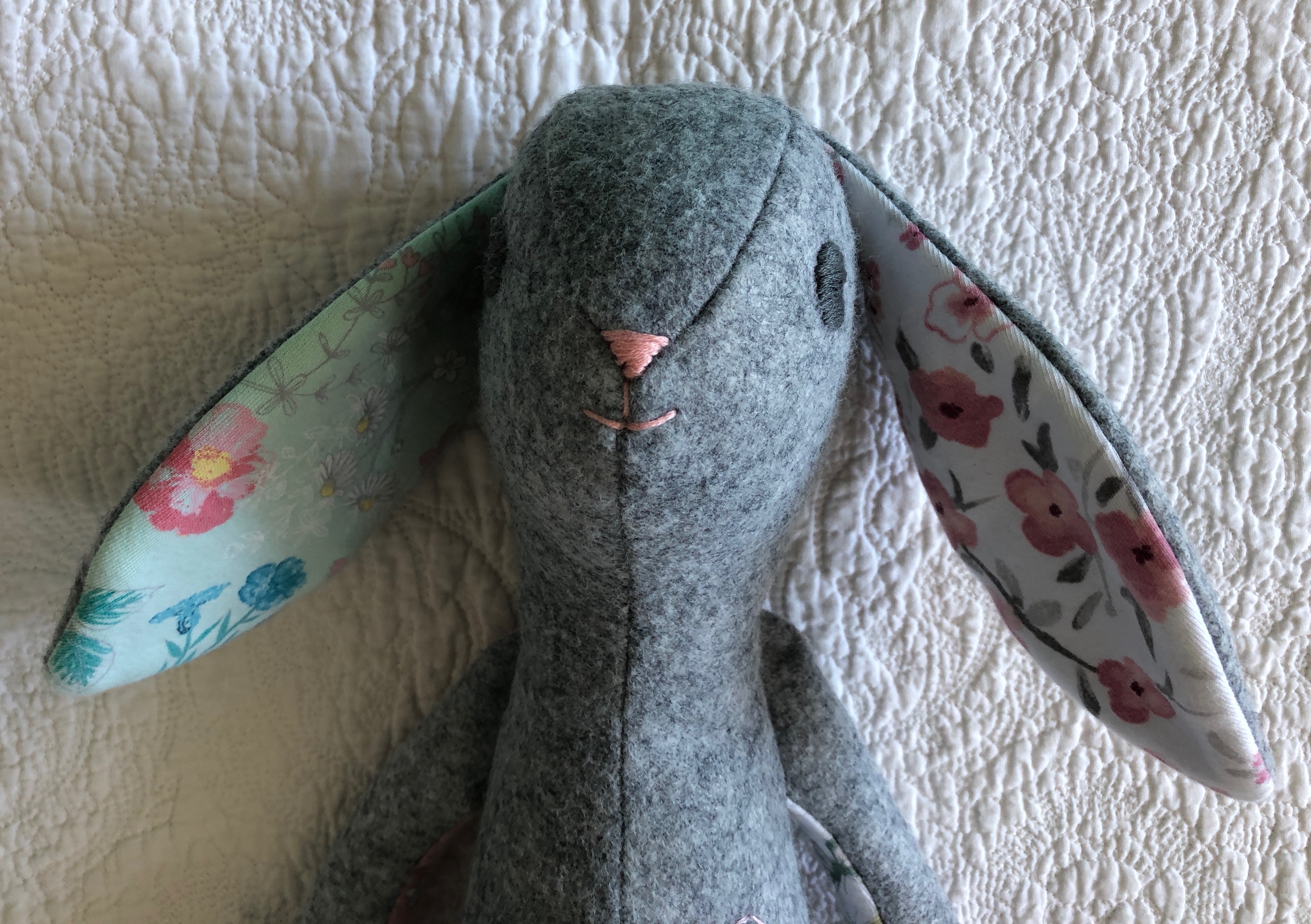 A grey felt and multi fabric keepsake bunny with hand embroidered details.