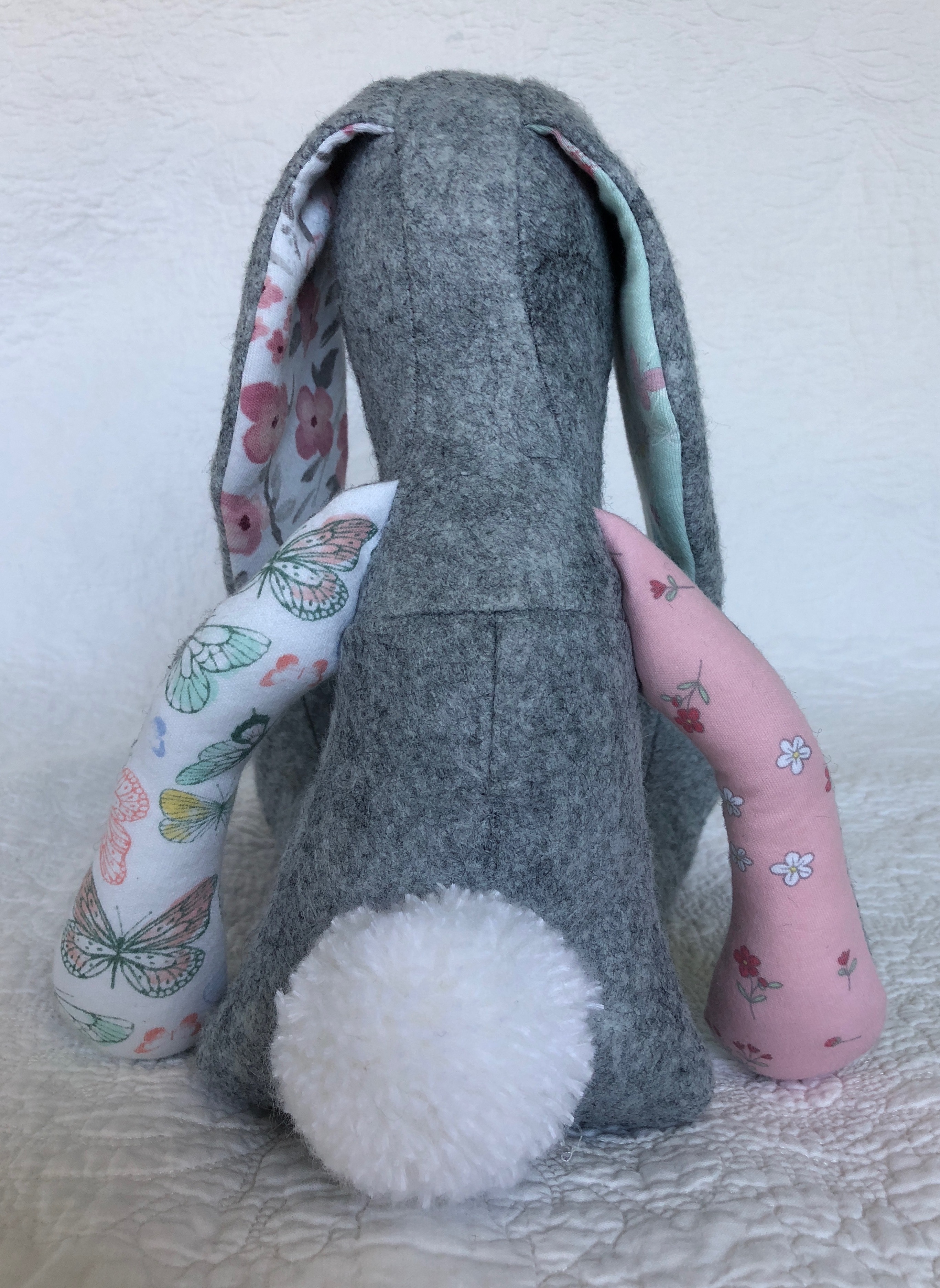 A grey felt and multi fabric keepsake bunny with hand embroidered details.