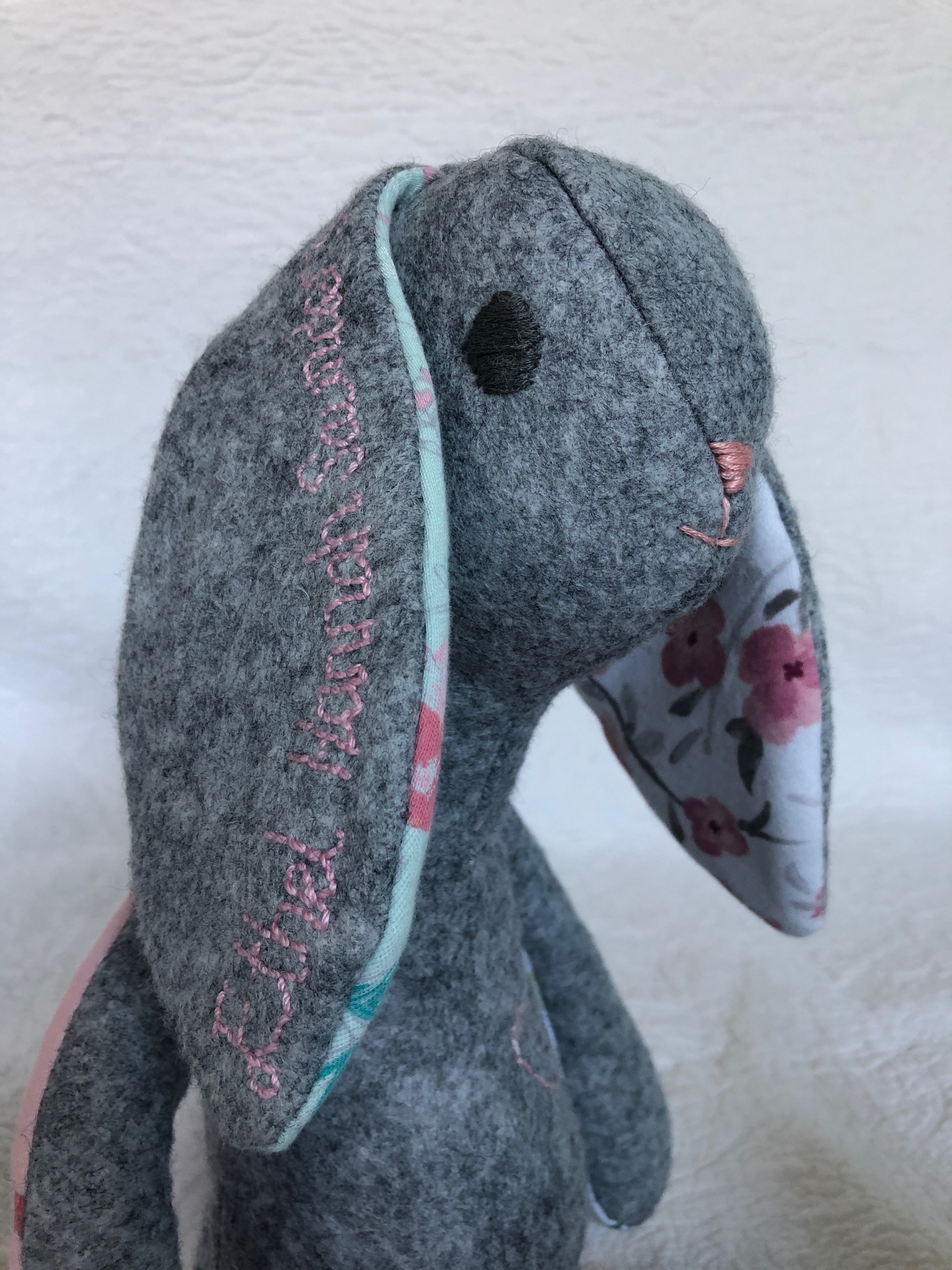 A grey felt and multi fabric keepsake bunny with hand embroidered details.