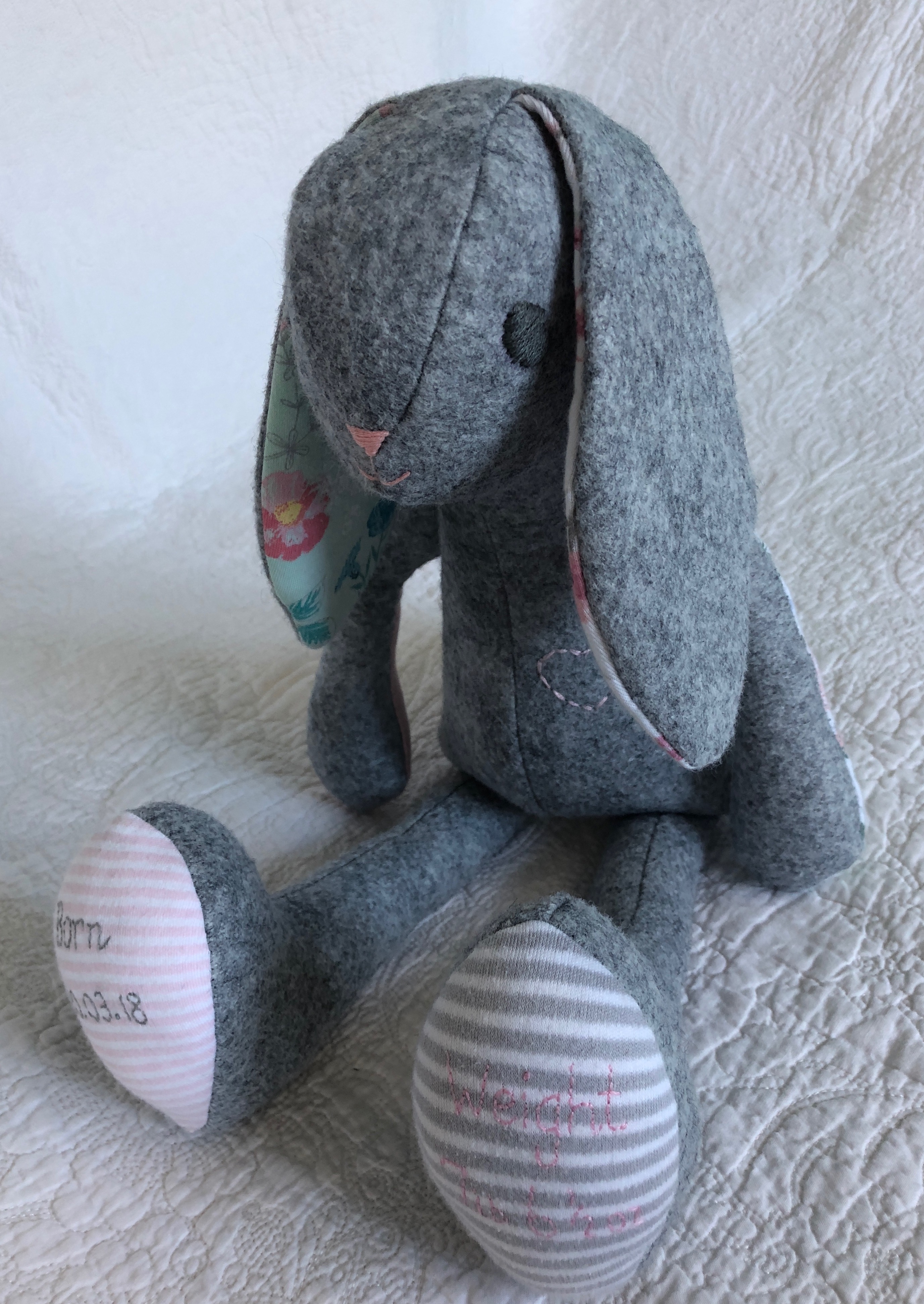 A grey felt and multi fabric keepsake bunny with hand embroidered details.
