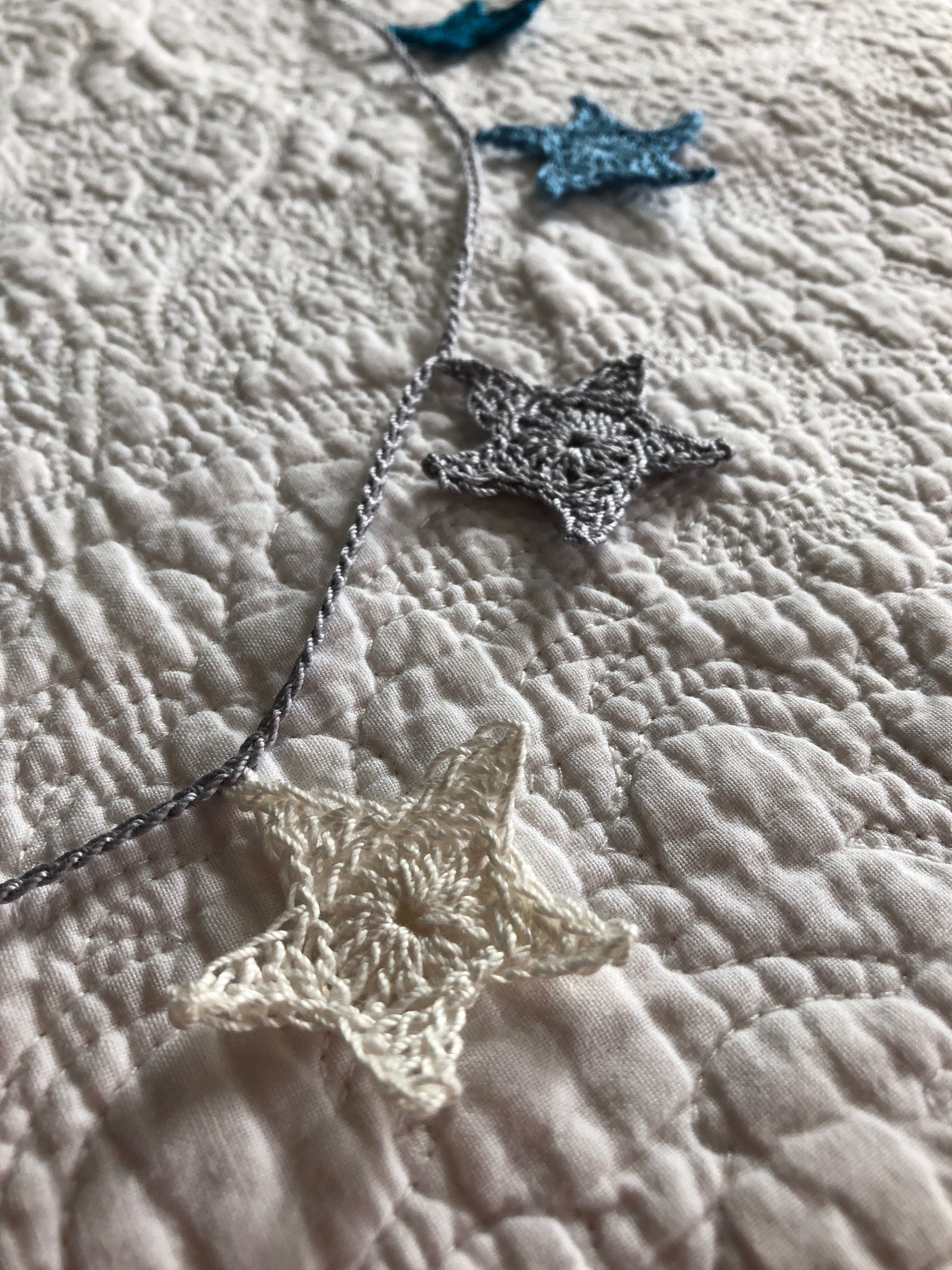 A small hand crocheted cotton star garland in petrol blue, mid blue, grey and white with a grey crocheted cord.