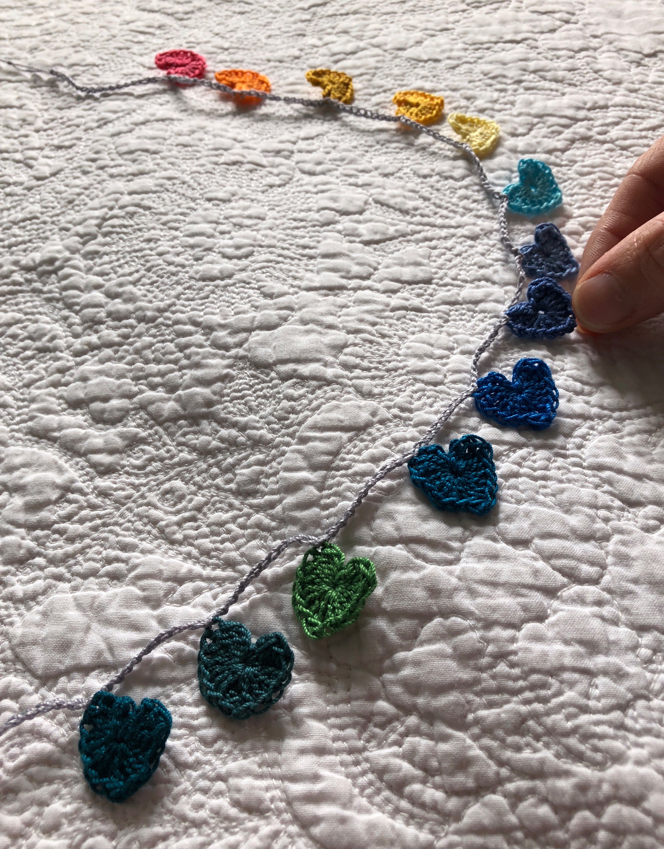 Tiny cotton crocheted hearts garland in a rainbow of colours grading from petrol blue through to pink.