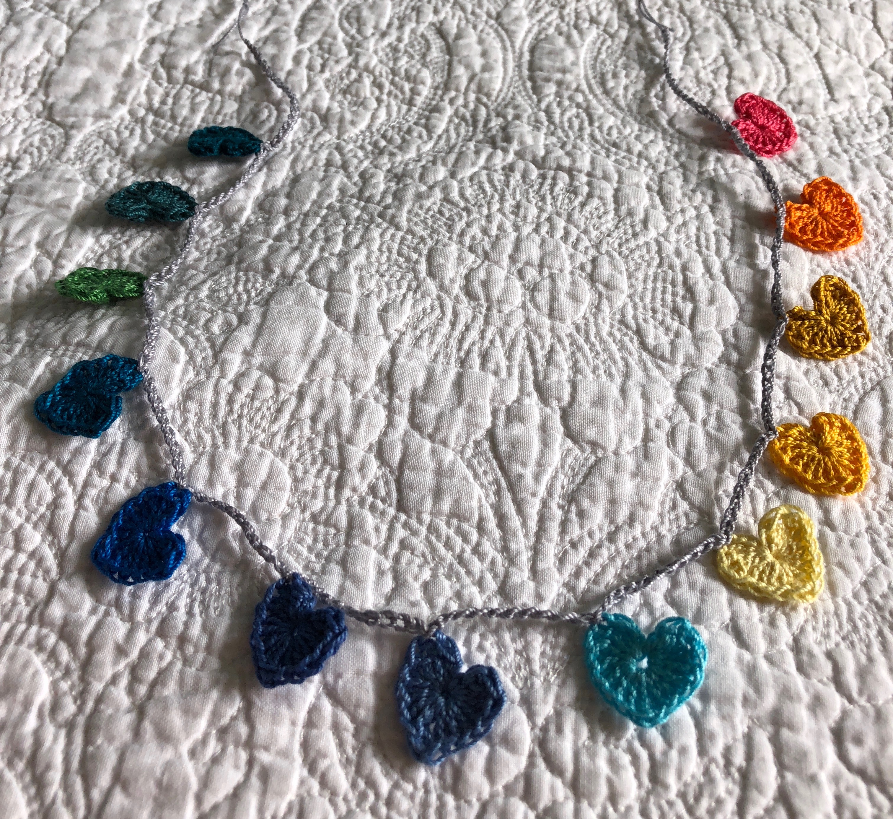 Tiny cotton crocheted hearts garland in a rainbow of colours grading from petrol blue through to pink.