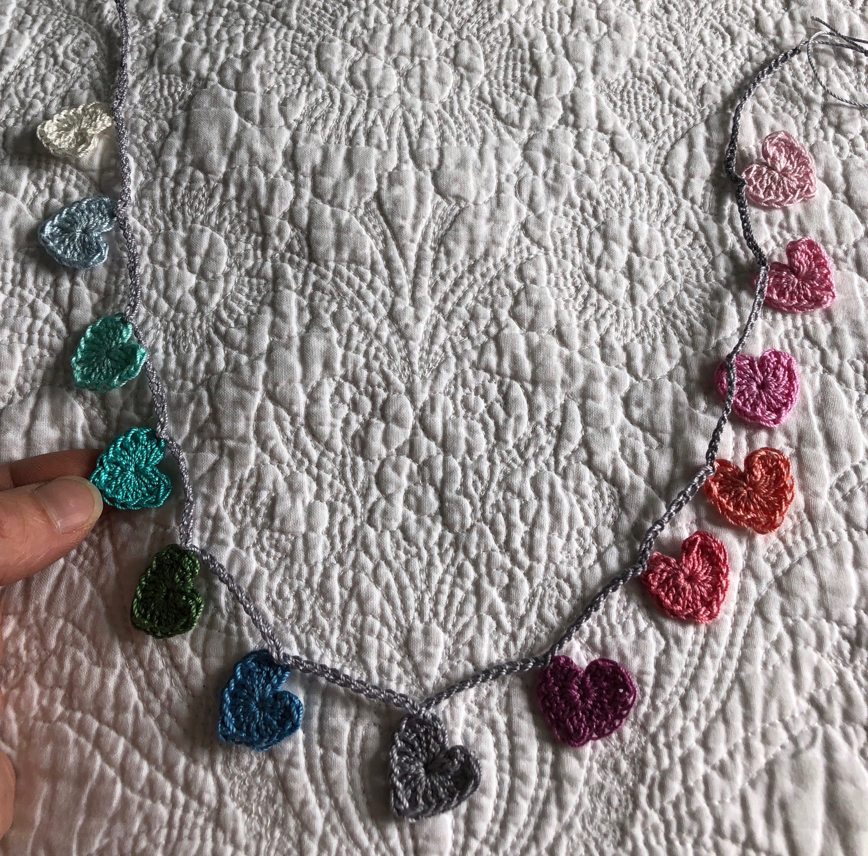 Tiny cotton crocheted hearts garland in a rainbow of pastel colours grading from white, pale blue through to pink.