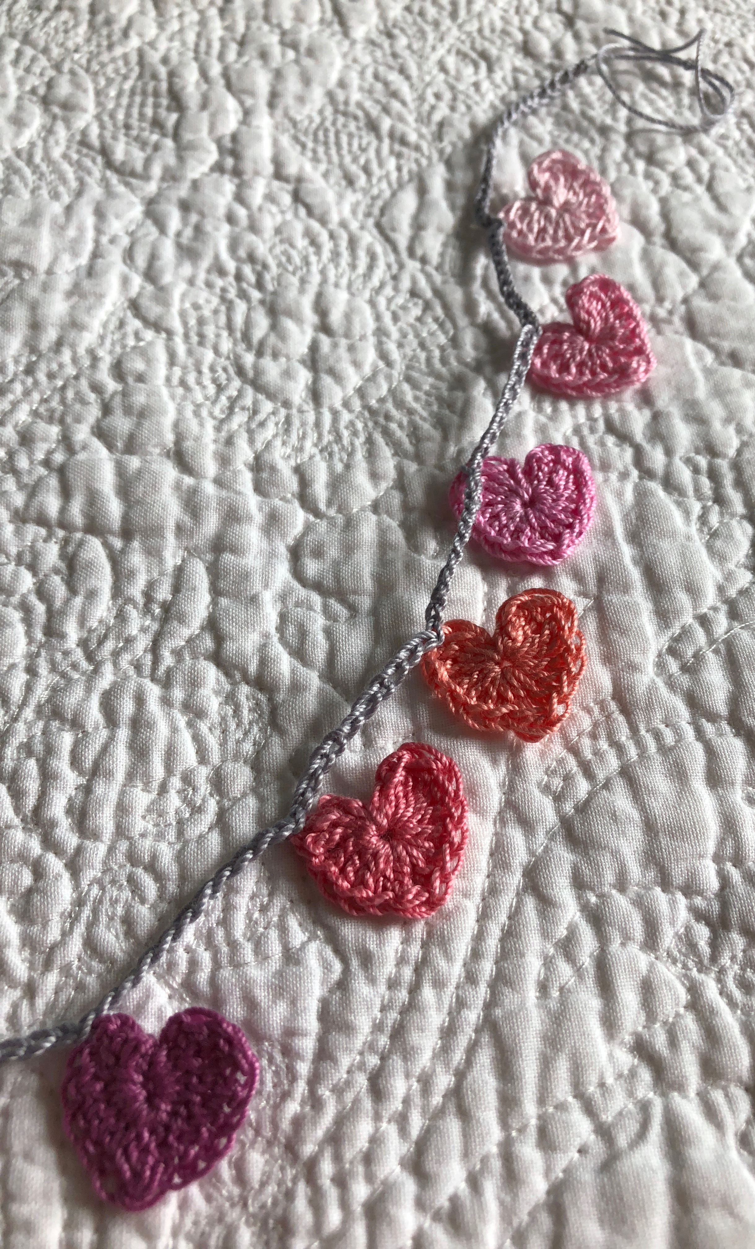 Tiny cotton crocheted hearts garland in a rainbow of pastel colours grading from white, pale blue through to pink.