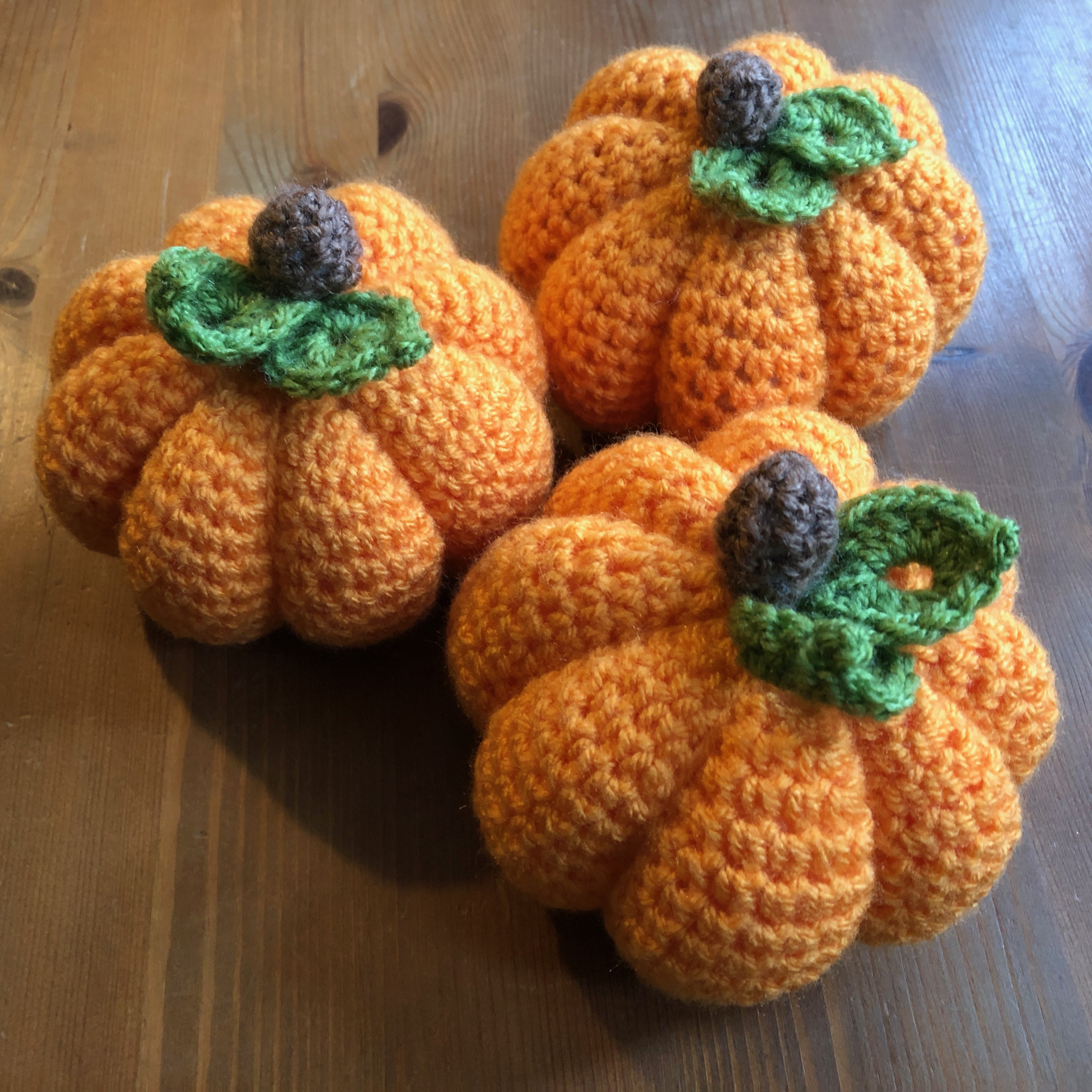 Hand made, crocheted pumpkins in orange, with brown stalk and green leaves.