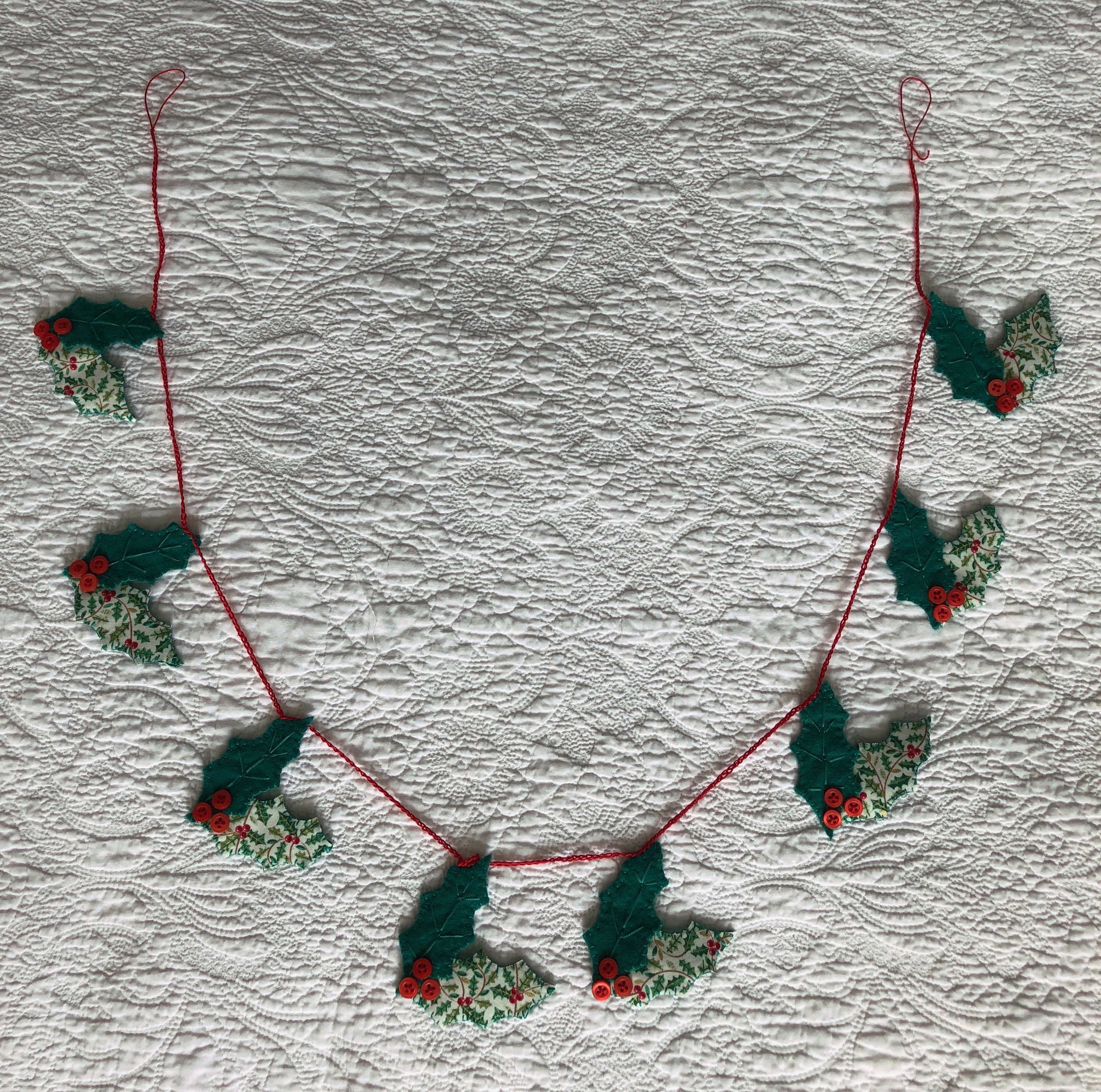 A handmade, hand stitched garland of green felt and holly printed cotton fabric holly leaves with red button berries.