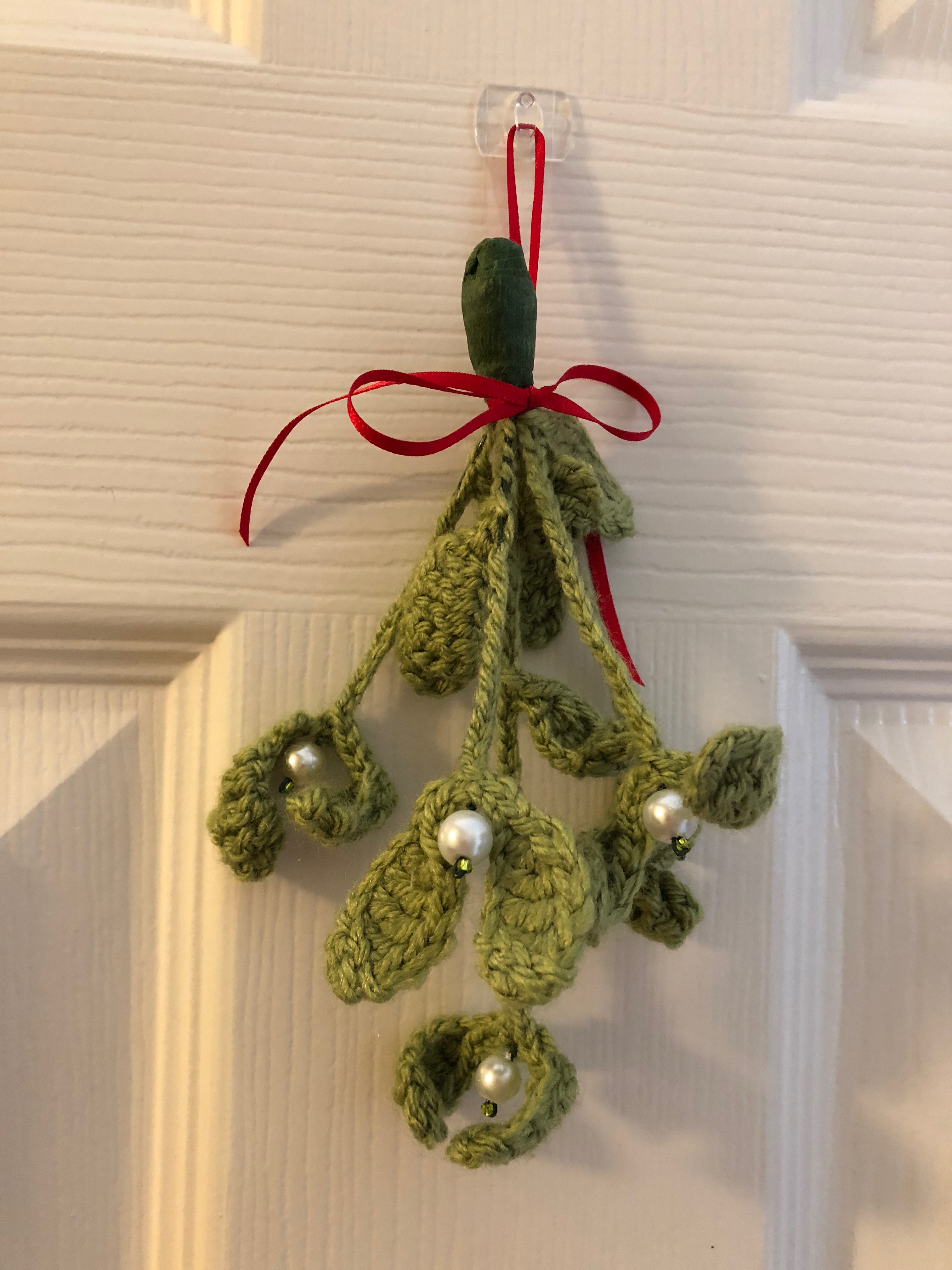 Handmade, crocheted bunch of wired green mistletoe, with white pearl and green glass bead berries and a red ribbon bow.