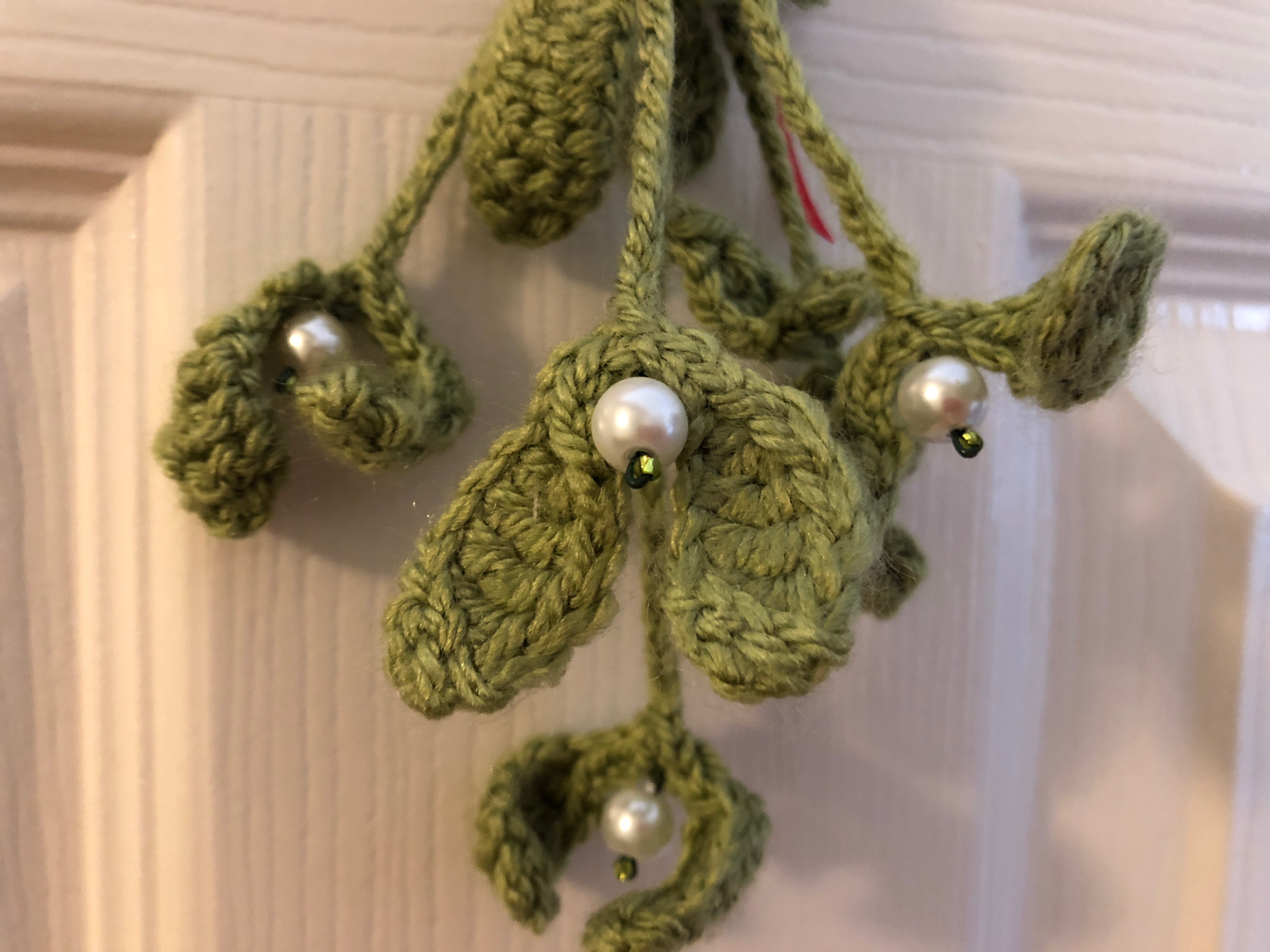 Handmade, crocheted bunch of wired green mistletoe, with white pearl and green glass bead berries and a red ribbon bow.