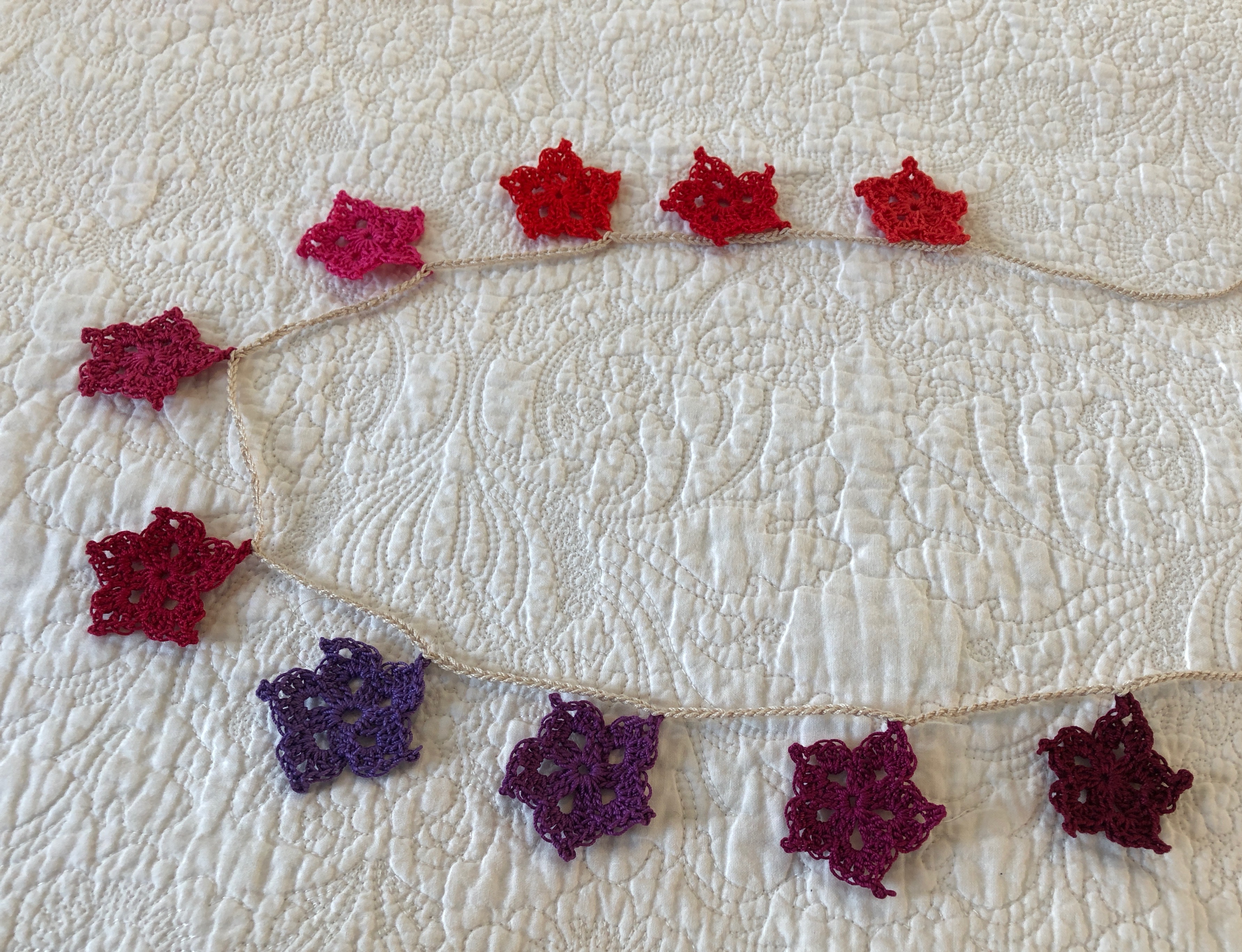 Hand made, crocheted, vintage style, cotton star garland in a gradient of red to purple shades.