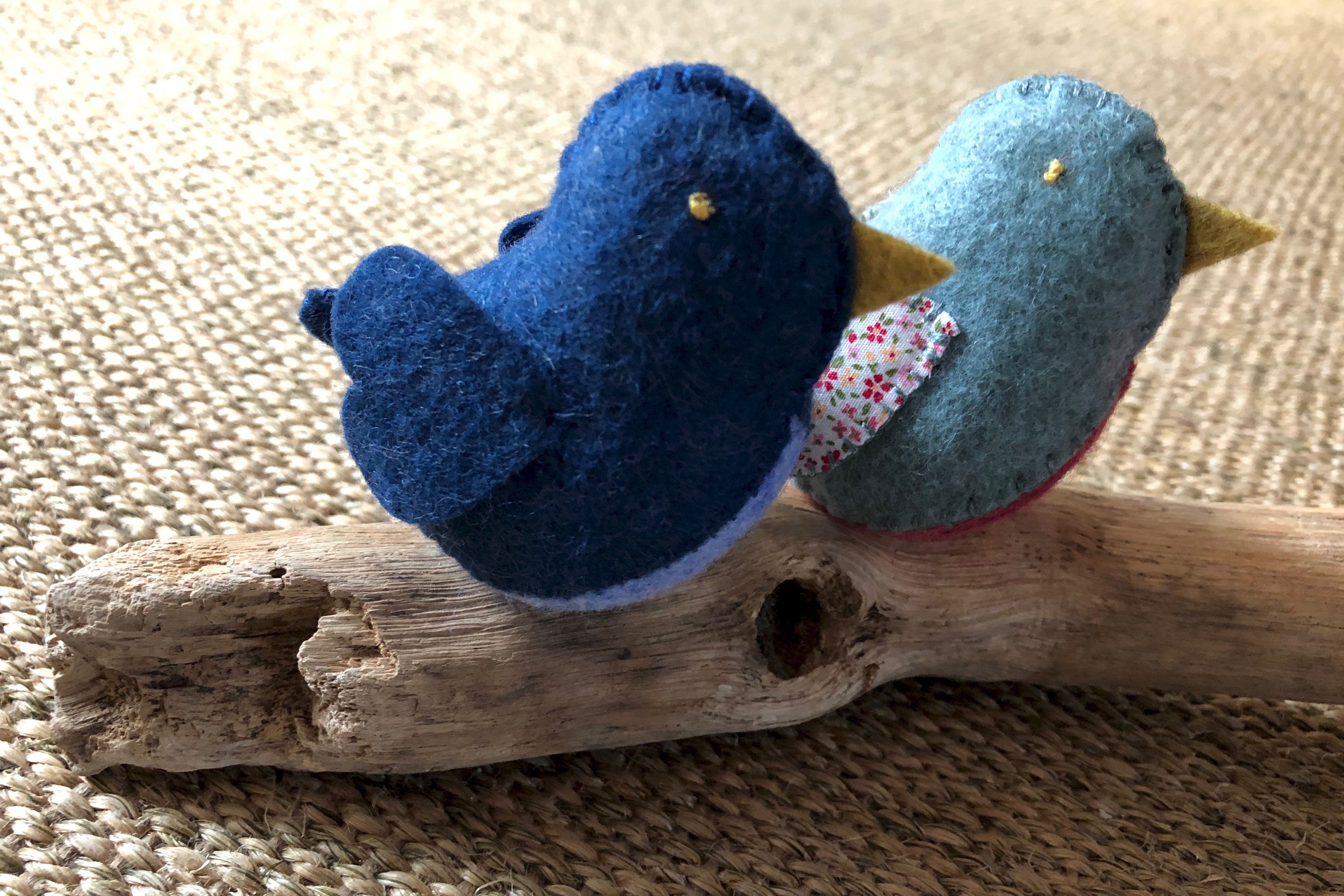 A family of 6 handmade and hand stitched felt and fabric birds sat on a drift wood log. Birds are made in a range of complimentary pastel shades of blue, green and pink with tiny flower fabric chests or wings.