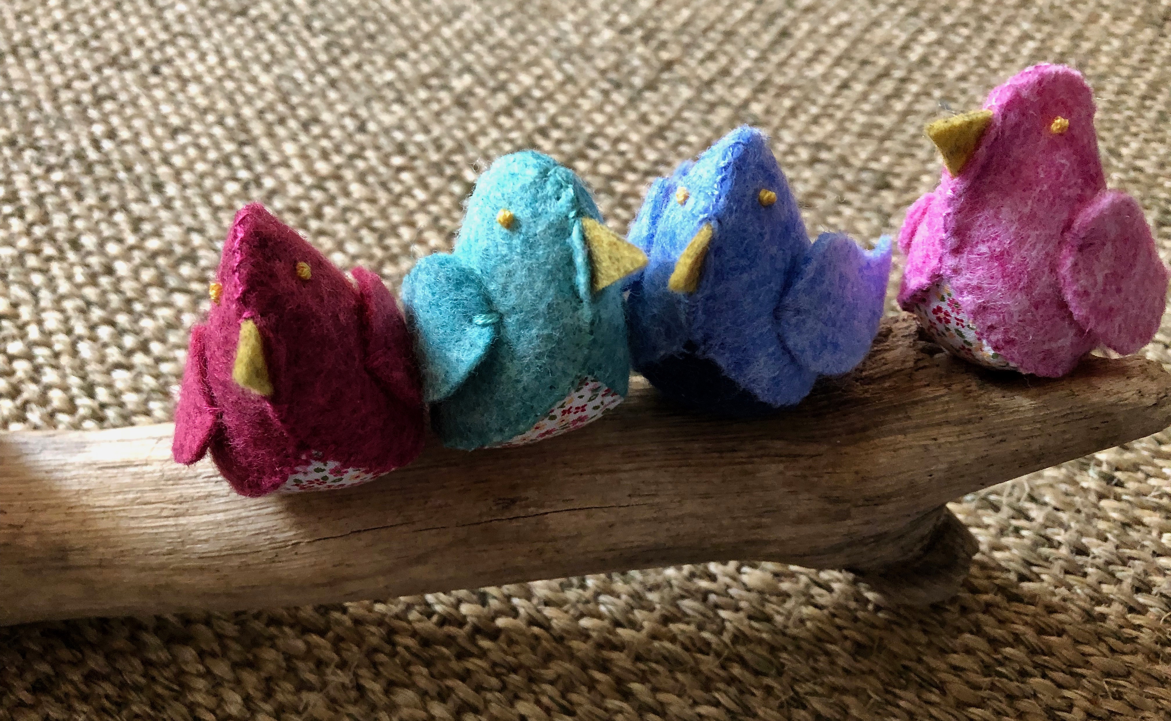 A family of 6 handmade and hand stitched felt and fabric birds sat on a drift wood log. Birds are made in a range of complimentary pastel shades of blue, green and pink with tiny flower fabric chests or wings.