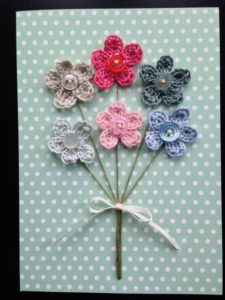 A posy of pastel coloured crocheted flowers with button centres on a spotty greetings card.