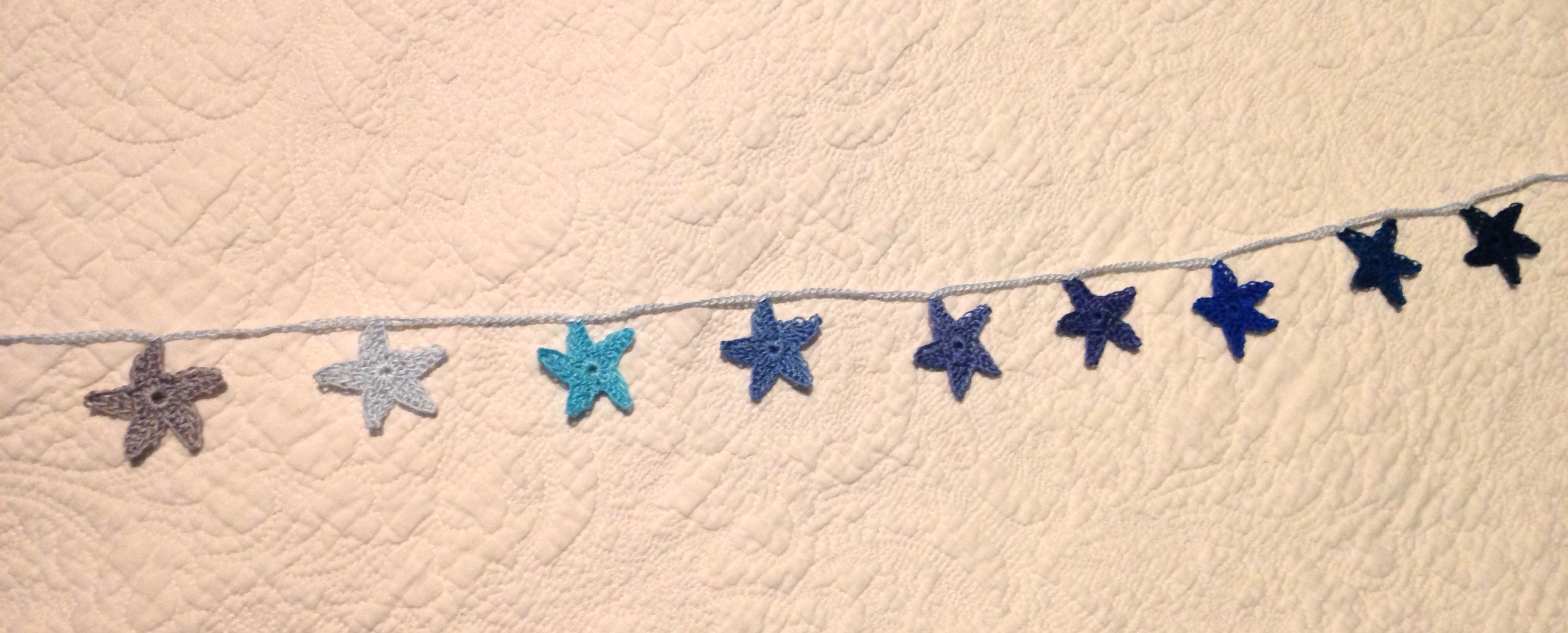 Hand crocheted mini star garland. A gradient of nine blue toned stars.