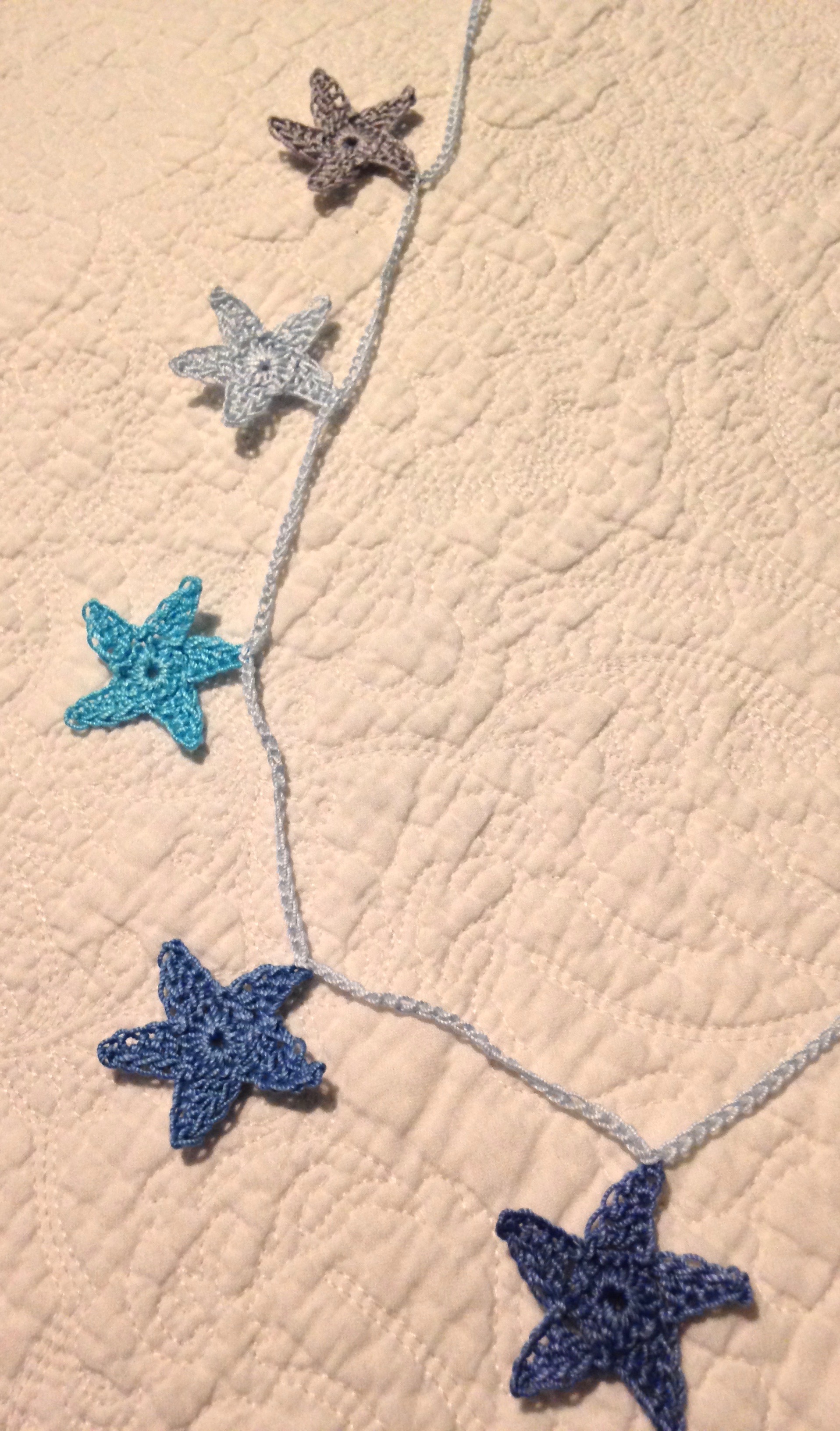 Hand crocheted mini star garland. A gradient of nine blue toned stars.