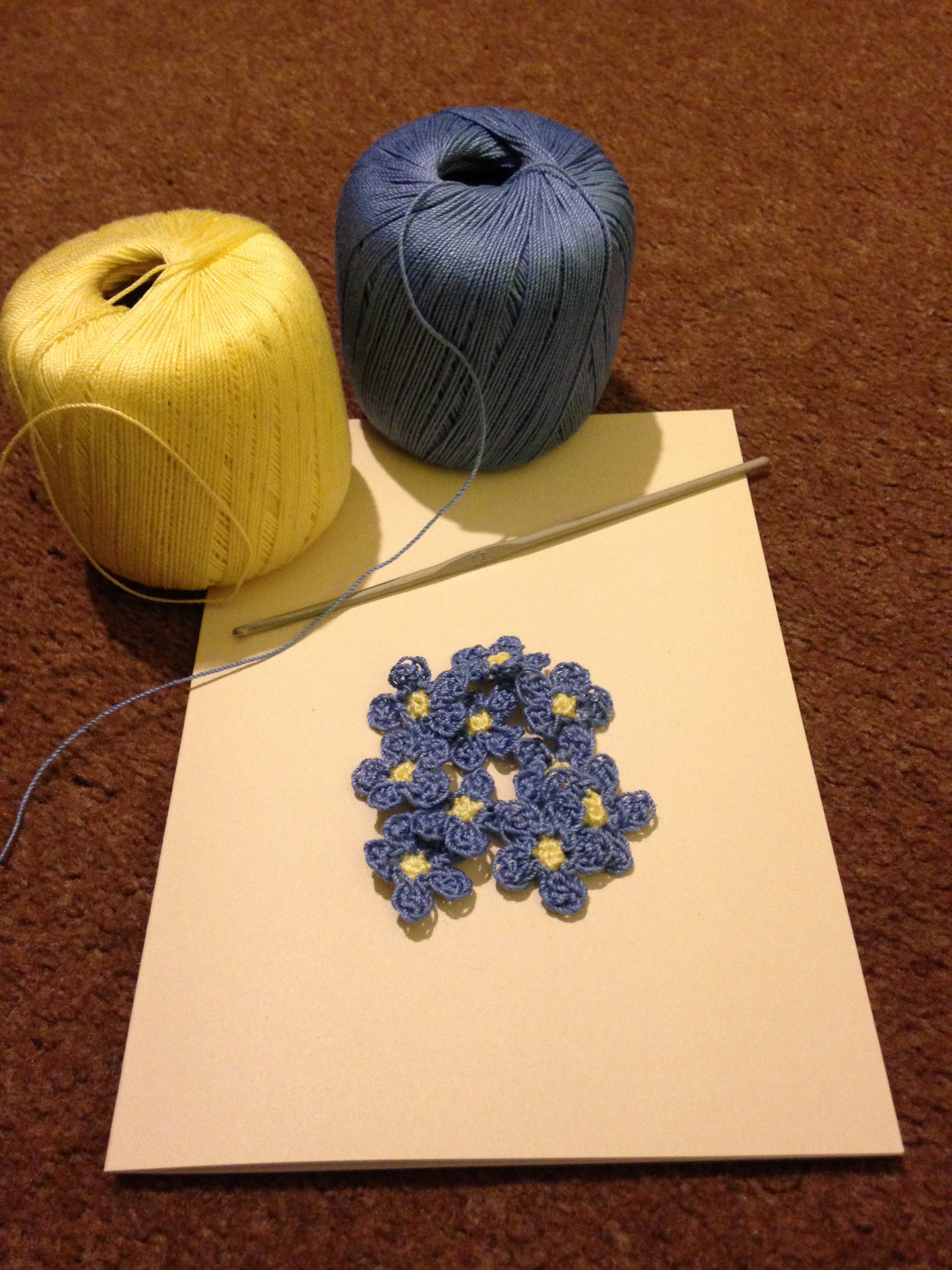 A hand stitched and crocheted greetings card with pale blue Forget-me-not flowers and green leaves.