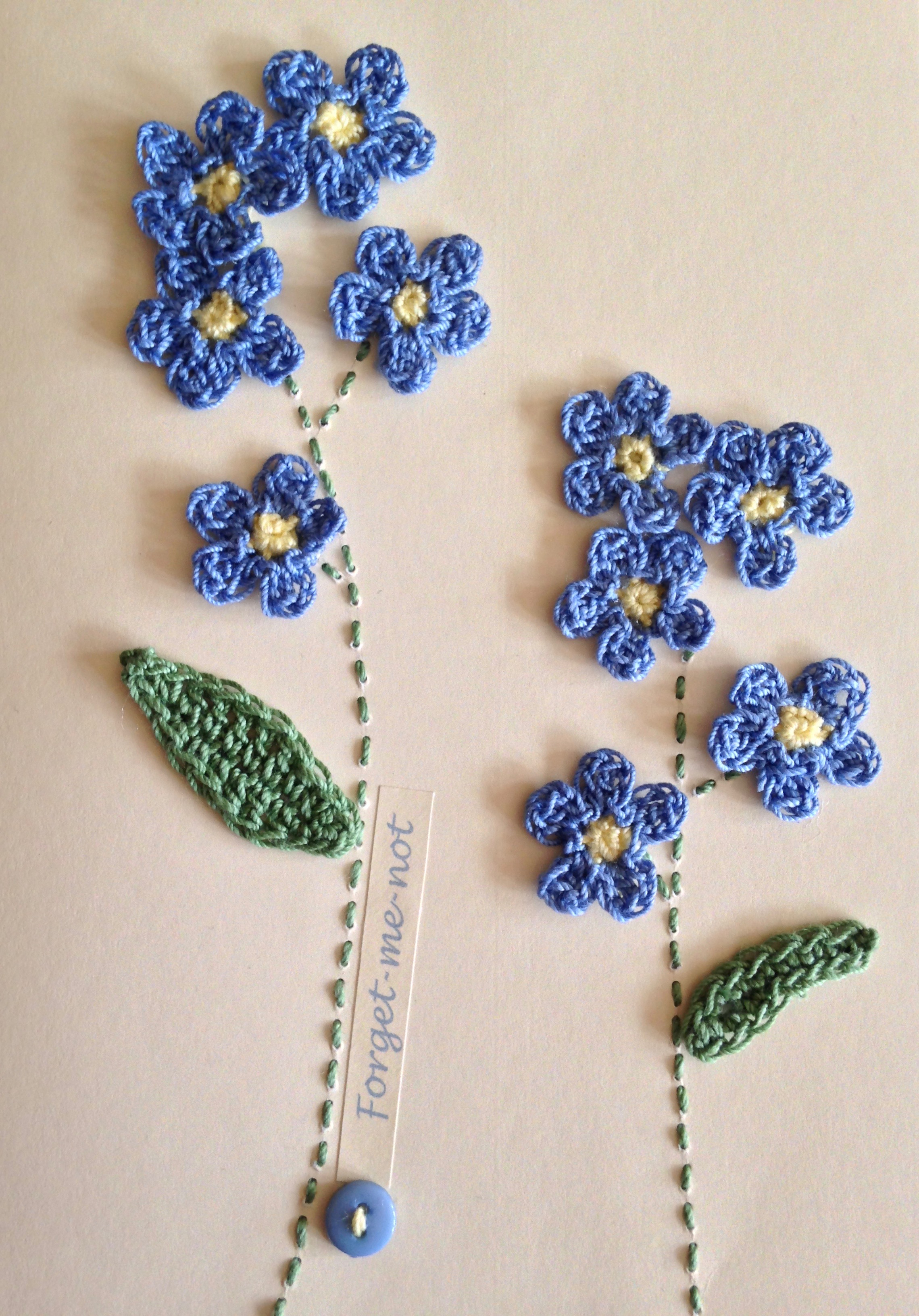 A hand stitched and crocheted greetings card with pale blue Forget-me-not flowers and green leaves.