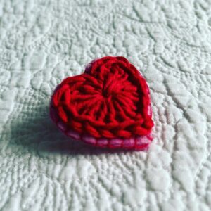 A small red crocheted heart on a pink hand stitched felt back with metal fixing brooch. Approximate size 4cm width x 4cm height.