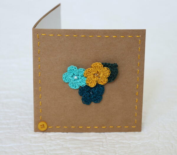 Posy of 3 crocheted flowers and a leaf with hand stitched border on a small brown card (approximate size 10 x 10 cm)with blank white insert. Brown envelope included.