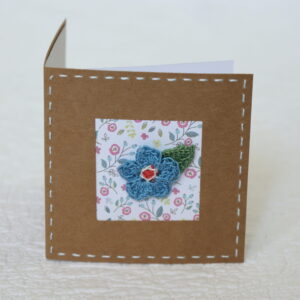 A single crocheted flower and a leaf with hand stitched border on a small brown card (approximate size 10 x 10 cm)with blank white insert. Brown envelope included.