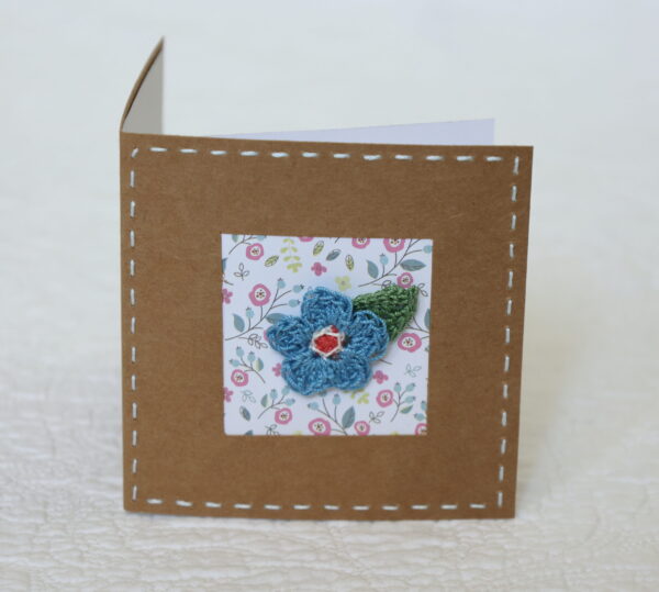 A single crocheted flower and a leaf with hand stitched border on a small brown card (approximate size 10 x 10 cm)with blank white insert. Brown envelope included.