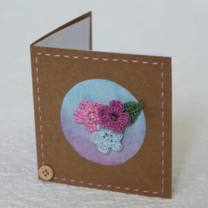 Posy of 3 crocheted flowers and a leaf with hand stitched border on a small brown card (approximate size 10 x 10 cm)with blank white insert. Brown envelope included.