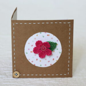 A single crocheted flower and a leaf with hand stitched border on a small brown card (approximate size 10 x 10 cm)with blank white insert. Brown envelope included.