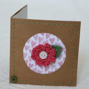 A single crocheted flower and a leaf with hand stitched border on a small brown card (approximate size 10 x 10 cm)with blank white insert. Brown envelope included.