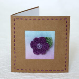 A single crocheted flower and a leaf with hand stitched border on a small brown card (approximate size 10 x 10 cm)with blank white insert. Brown envelope included.
