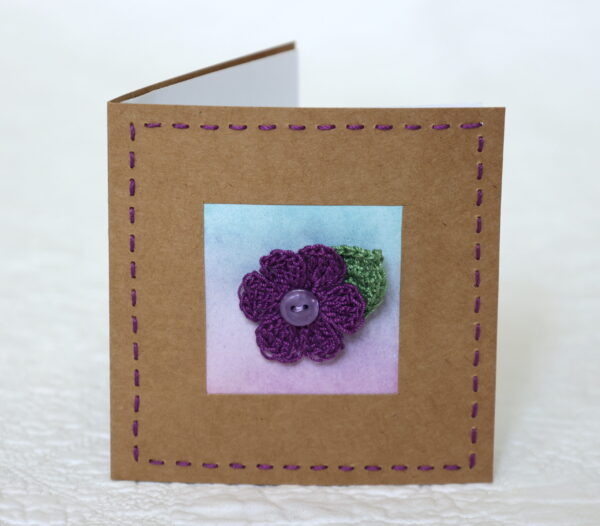 A single crocheted flower and a leaf with hand stitched border on a small brown card (approximate size 10 x 10 cm)with blank white insert. Brown envelope included.