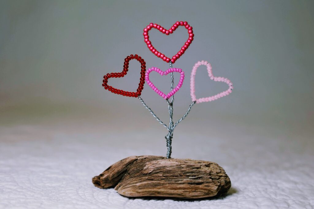 A small free standing decoration of a red and pink glass bead and wire hearts on a natural driftwood base.