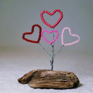 A small free standing decoration of a red and pink glass bead and wire hearts on a natural driftwood base.