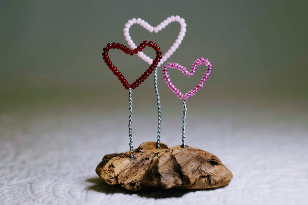 A small free standing decoration of a red, pink and purple glass bead and wire hearts on a natural driftwood base.