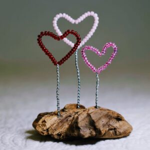 A small free standing decoration of a red, pink and purple glass bead and wire hearts on a natural driftwood base.