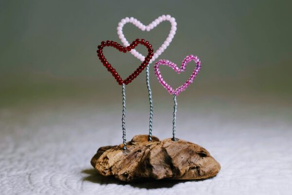 A small free standing decoration of a red, pink and purple glass bead and wire hearts on a natural driftwood base.