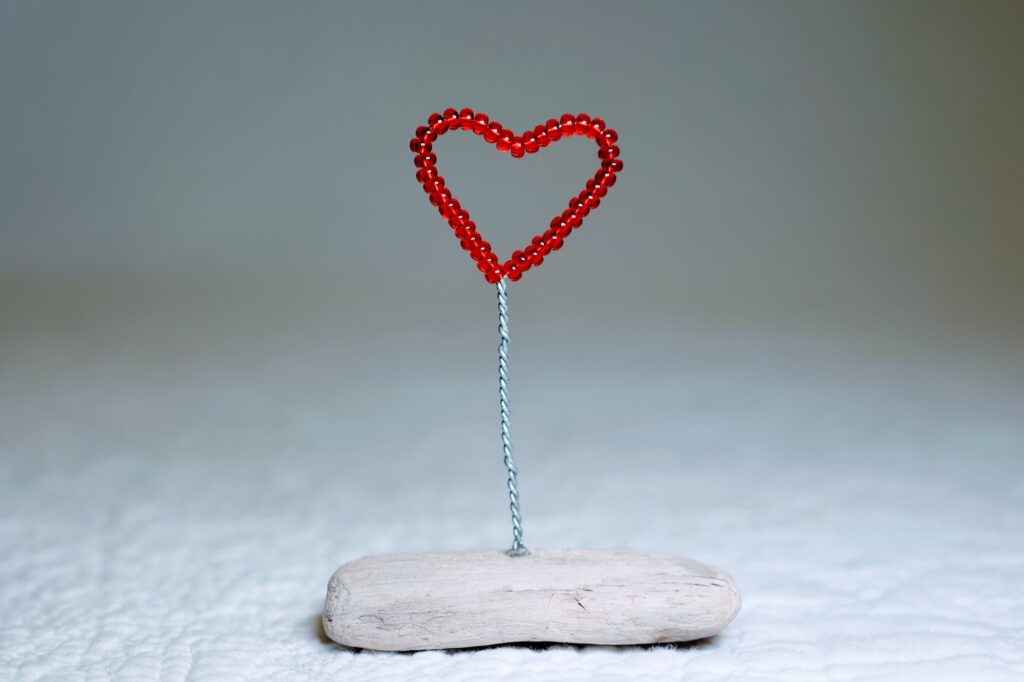 A small, red glass bead and wire heart on a natural driftwood base.