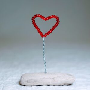 A small, red glass bead and wire heart on a natural driftwood base.