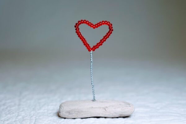 A small, red glass bead and wire heart on a natural driftwood base.