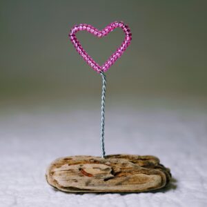 A small, pink glass bead and wire heart on a natural driftwood base.