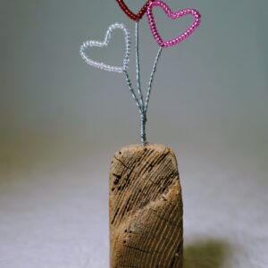 A small free standing decoration of a red, pink and clear glass bead and wire hearts on a natural driftwood base.