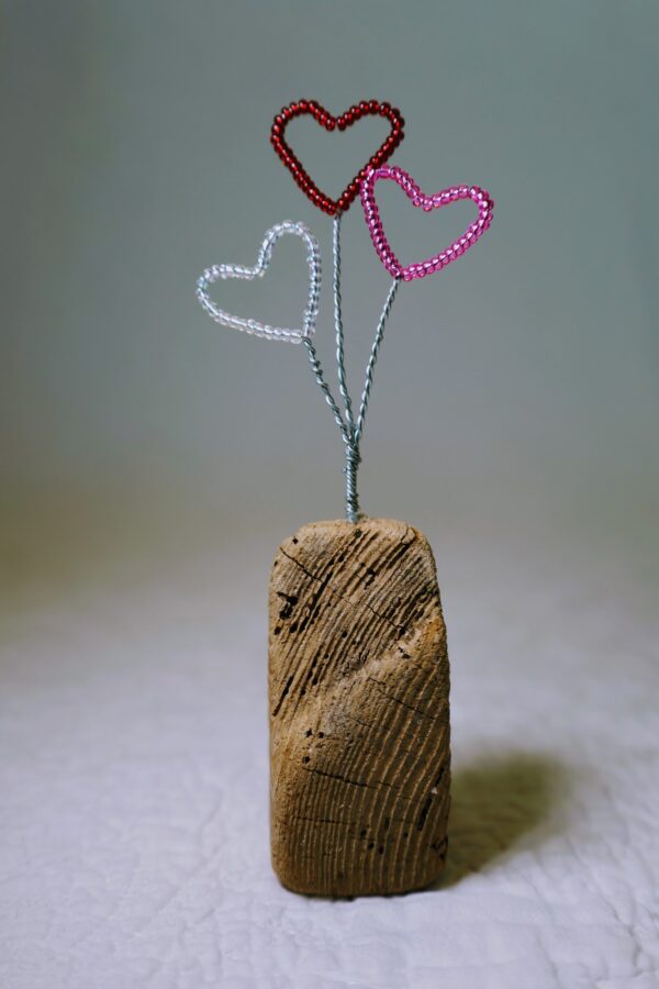 A small free standing decoration of a red, pink and clear glass bead and wire hearts on a natural driftwood base.