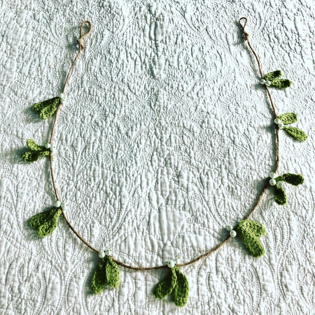 A hand crocheted mistletoe and beaded garland on jute.